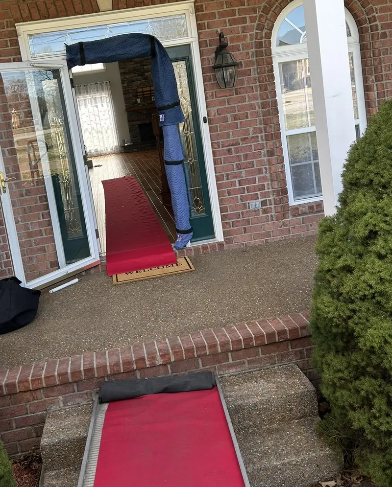 A front doorway prepared for a move: moving pads wrapped around the door frame and a red runner laid across the floor, porch and steps.