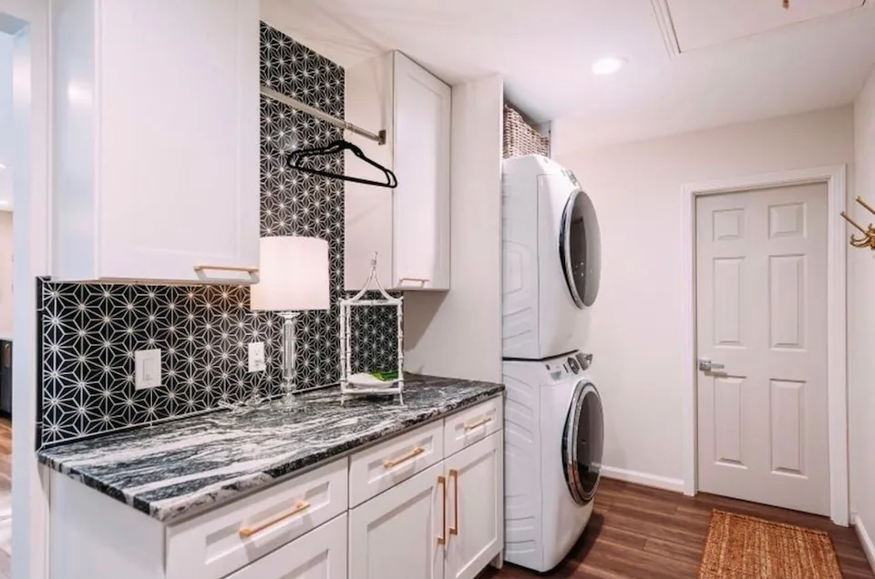 A laundry area with a stacked washer and dryer, cabinets and a patterned backsplash.