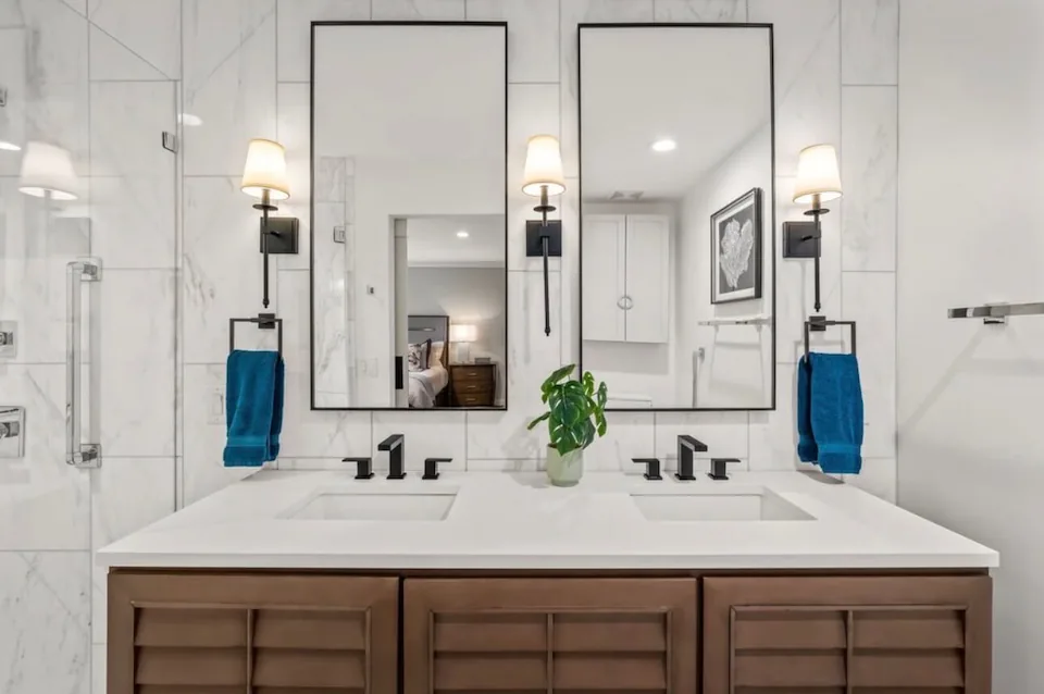A bathroom with a double vanity, two framed mirrors and wall sconces.
