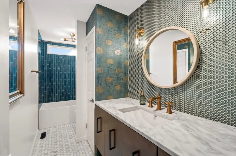 A bathroom with patterned tile, a round mirror and a marble-topped vanity.