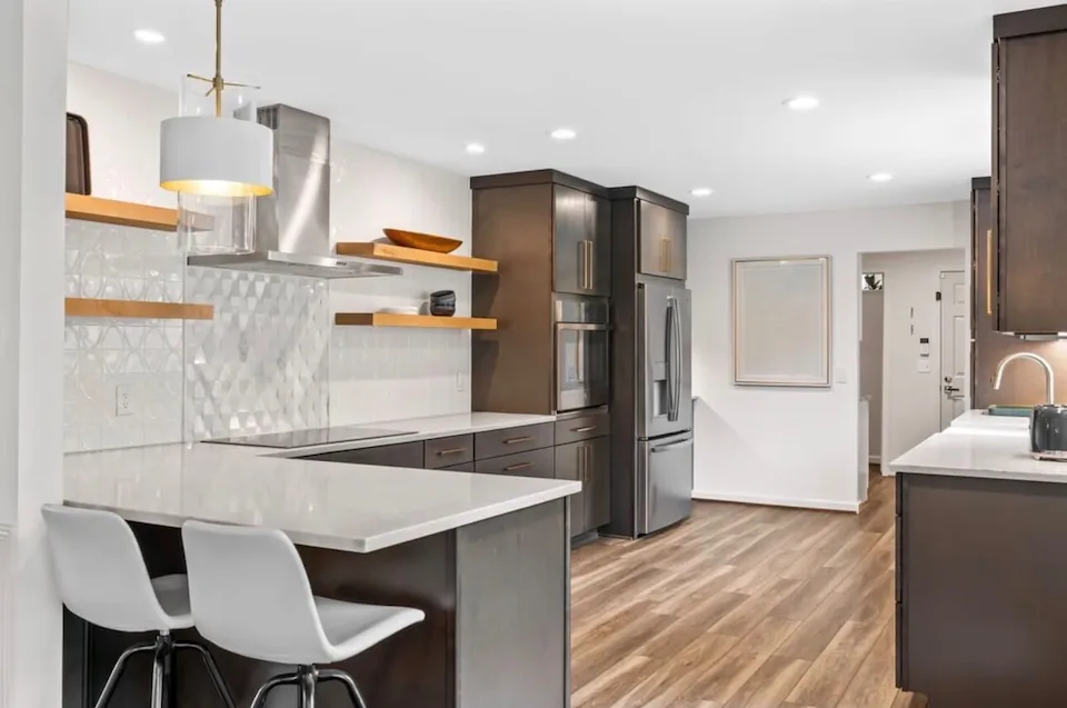 An open kitchen with a breakfast bar, white stools and open shelving.