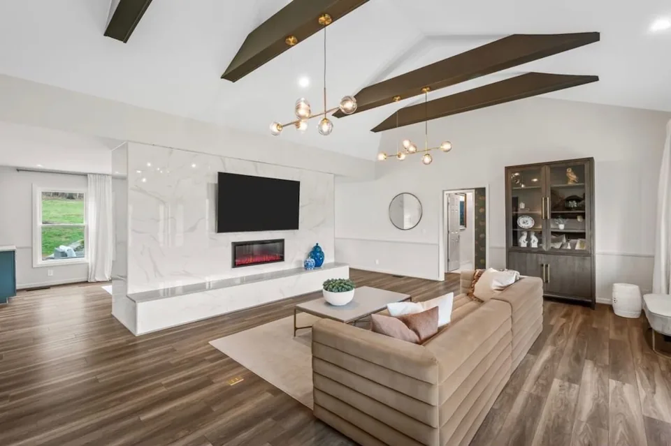 A living room with a fireplace wall, mounted TV and exposed ceiling beams.